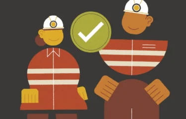 Stylised illustration of two smiling workers wearing orange safety uniforms and white helmets, standing side by side with a large green checkmark between them, symbolising safety approval.